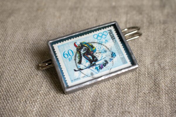 Dzikie Twory - broszka ze znaczkiem pocztowym z 1968 roku - Igrzyska Olimpijskie w Grenoble zjazd narciarski, przód broszki